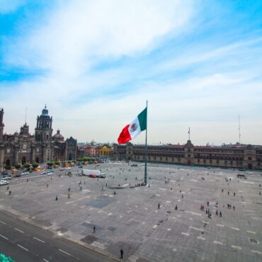 Mexican flag waving in Mexico’s centro histórico with cathedral and presidential palace in the back.